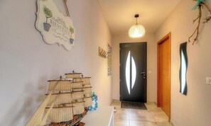 A hallway with a ship model, a welcome sign, a door, and a pendant light. - VILLA LES PINS DE BONIFACIO (BONIFACIO)