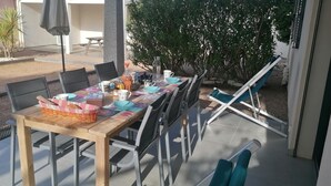 Een buitenterras met een lange tafel, stoelen en een bank.