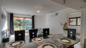 Un área de comedor con una mesa redonda dispuesta para cuatro, un sofá al fondo y vistas a espacios verdes.