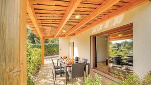 Un porche cubierto con una mesa dispuesta para el desayuno, una puerta corrediza de vidrio que da a un jardín y una estructura de techo de madera.