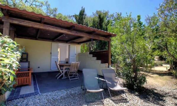 A covered outdoor seating area with a table and chairs, a small wooden bench, and a door leading to an interior space. - Tilleul 1 - COSTA - Gîte (COSTA)