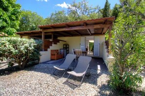 Un'area salotto esterna coperta con due poltrone, un pergolato in legno e una scala che conduce a una porta.