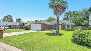 A residential neighborhood with houses, a palm tree, and a well-maintained lawn. - Anchors Up | Private Pool | Kayaks | Outdoor Games | My Beach Getawys (Pensacola)