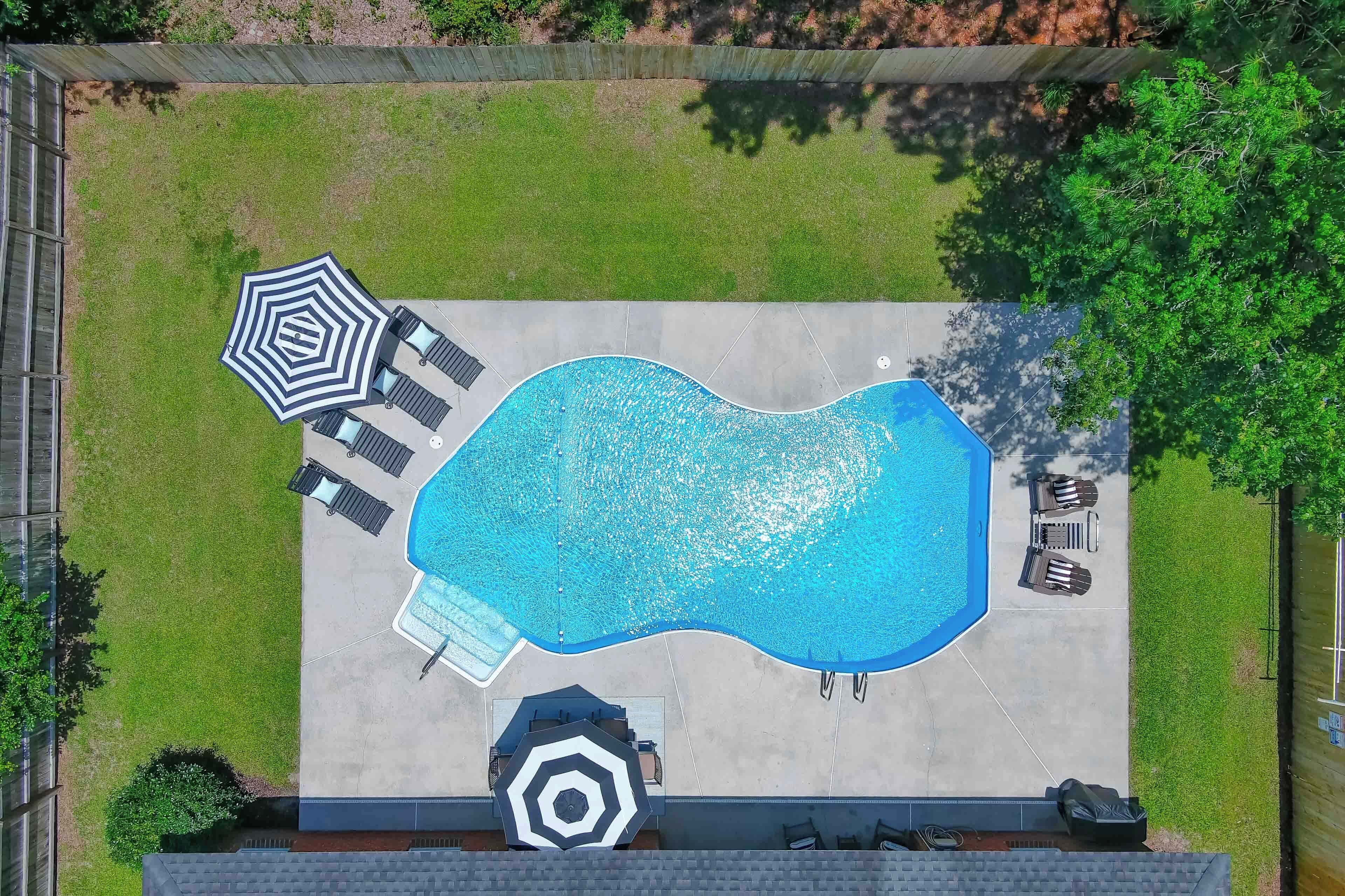 Une vue aérienne d’une piscine entourée de chaises longues et de parasols, le tout délimité par une clôture.