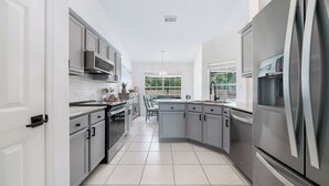 Una cocina moderna con armarios grises, electrodomésticos de acero inoxidable y piso de baldosas.