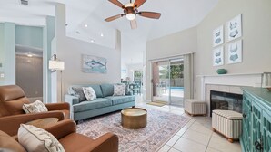 Una sala de estar con sofá, sillón y reposapiés, ventilador de techo y chimenea.