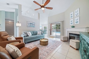 A living room with a sofa, armchair, and ottoman, a ceiling fan, and a fireplace.