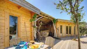 Una cabaña de madera con terraza, una mesa de comedor con sillas y un pequeño jardín.