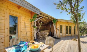 Eine Holzlaube mit einer Terrasse, einem Esstisch mit Stühlen und einem kleinen Garten.