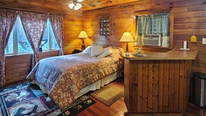 Un dormitorio de cabaña de madera con cama, lámparas de noche, tocador y ventilador de techo.