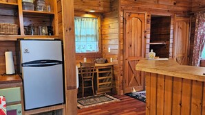 Interior de una cabaña de madera con refrigerador, armarios de madera, una mesa de comedor y una zona de bar.