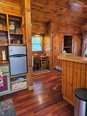 A wooden cabin interior with a refrigerator, wooden cabinets, a dining table, and a bar area. - Adorable 1-bedroom cabin with AC in welcoming Bryson City (Bryson City)