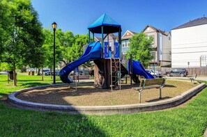 A playground with slides and a covered play structure, surrounded by grass and trees. - Pet-Friendly Parkfront Home - Yard & Rooftop Views (Houston)