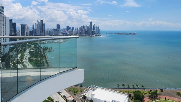 A high-rise building with a glass balcony overlooking a city skyline and a body of water. - Room-luxury Oceanview Room Rooftop P (Panama City)