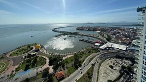 An aerial view of a coastal city with a marina, a curved road, and a large building with a sloped roof. - Room-luxury Oceanview Room Rooftop P (Panama City)