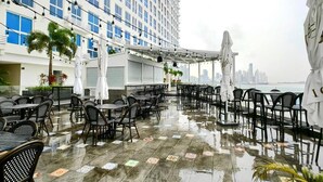 An outdoor terrace with tables and chairs, umbrellas, and a view of a city skyline. - Room-luxury Oceanview Room Rooftop P (Panama City)