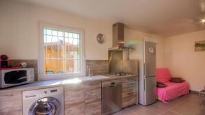 Uma cozinha compacta com máquina de lavar, micro-ondas e lava-louças, uma janela com grades, um relógio e um sofá revestido de rosa.