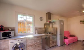 A compact kitchen with a washing machine, microwave, and dishwasher, a window with bars, a clock, and a pink-covered sofa. - Ermiccia - PATRIMONIO (PATRIMONIO)
