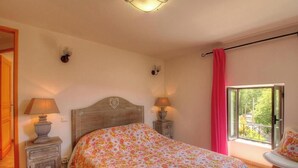Een slaapkamer met een bed, twee bedlampen, een raam met uitzicht en een stoel.