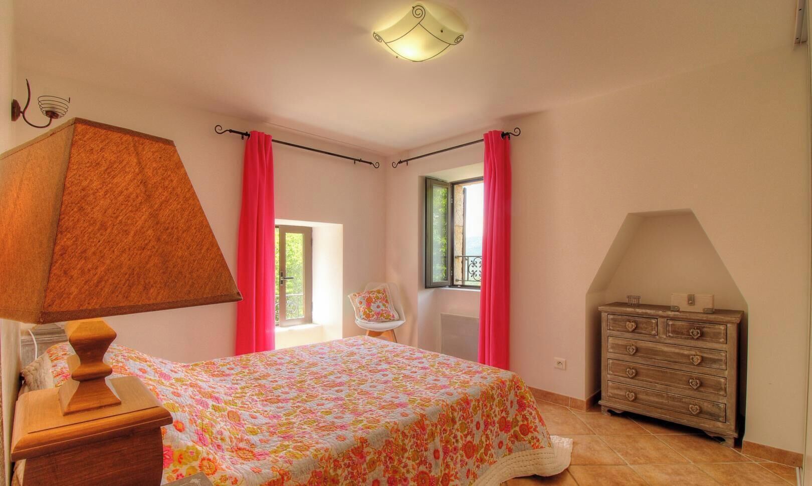 Une chambre à coucher avec un lit, une commode, une chaise et une fenêtre avec des rideaux.