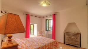 Een slaapkamer met een bed, een dressoir, een stoel en een raam met gordijnen.
