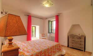 Ein Schlafzimmer mit Bett, Kommode, Stuhl und einem Fenster mit Vorhängen.