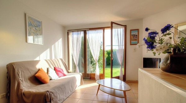 Ein Wohnzimmer mit einer Couch, einem kleinen Tisch, einem Fernseher und Blick ins Freie durch eine Schiebetür.