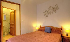 Ein Schlafzimmer mit Bett, Nachttisch, Wandlampe, einer Tür zu einem Badezimmer und einer Wanddekoration.