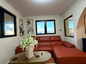 A living room with a red sofa, a round wooden table, and a vase of flowers.