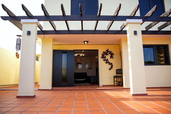 A building entrance with a tiled patio, a dark door, and a wall-mounted decorative item. - Tropical villa with heated pool & panoramic views (Luquillo)