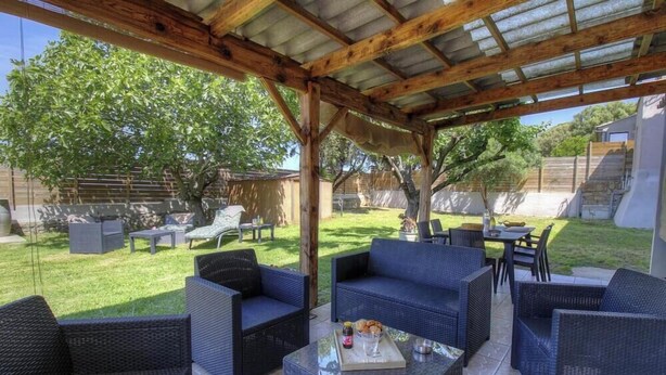 Veranda esterna coperta con mobili in vimini, un tavolo con un vassoio di snack e un prato sullo sfondo.