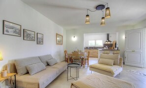 Ein Wohnzimmer mit einer Couch, einem Esstisch und Stühlen. Im Hintergrund ist eine Küche zu sehen.
