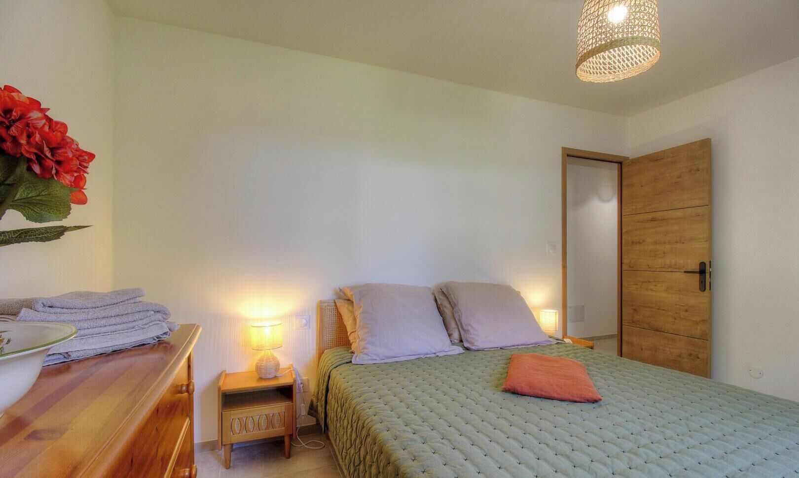 Une chambre à coucher comprenant un lit, des tables de chevet, une lampe, une armoire en bois et un luminaire suspendu.