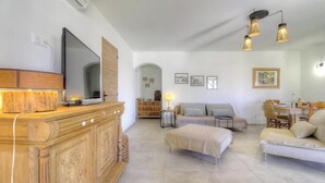 Un soggiorno moderno con televisione a schermo piatto, mobiletto in legno, divano, poggiapiedi, tavolo da pranzo e lampade a parete.