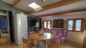 A dining area with a round wooden table, chairs, a television, and a sofa with a view of the outdoors. - Nanu - AULLENE - Gîte (AULLENE)