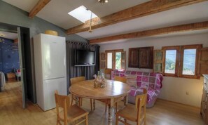 A dining area with a round wooden table, chairs, a television, and a sofa with a view of the outdoors. - Nanu - AULLENE - Gîte (AULLENE)