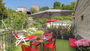 An outdoor patio with red chairs and tables, a large umbrella, and a stone building in the background. - Nanu - AULLENE - Gîte (AULLENE)