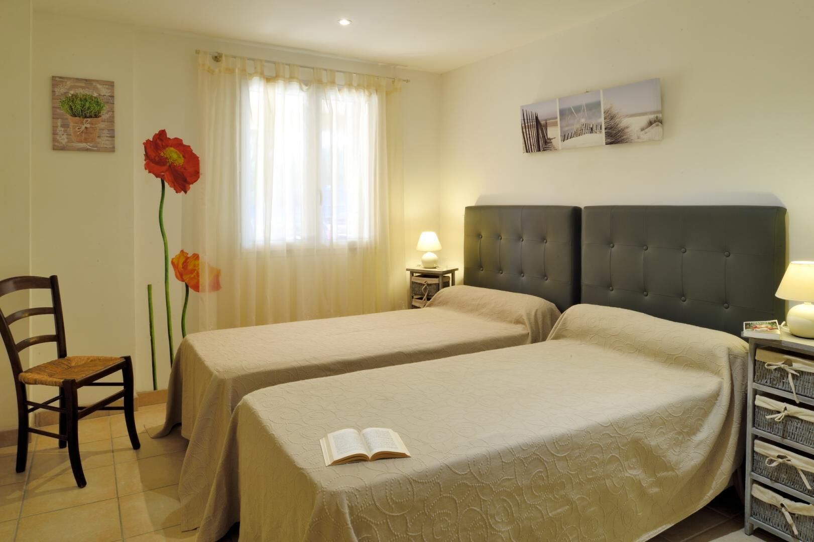 Une chambre d’hôtel avec deux lits, une chaise, une lampe et des œuvres d’art accrochées aux murs.