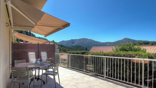 A balcony with a table and chairs, a white railing, and a view of mountains. - U Castagnu 2 - EVISA (EVISA)