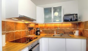 A modern kitchen with a wooden countertop, stainless steel appliances, and a backsplash of orange tiles. - U Castagnu 2 - EVISA (EVISA)