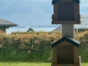 Una estructura de madera con techo oscuro, rodeada de vegetación y vistas a un cuerpo de agua con edificios al fondo.