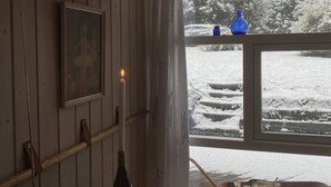 A room with a framed picture on the wall, a candle, a bottle, and a window with a view of snow-covered steps and trees. - 4 Star Holiday Home in Kalundborg (Kalundborg)