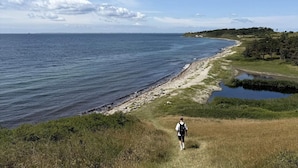 A coastal landscape with a person walking along a grassy path beside a body of water. - 4 Star Holiday Home in Kalundborg (Kalundborg)