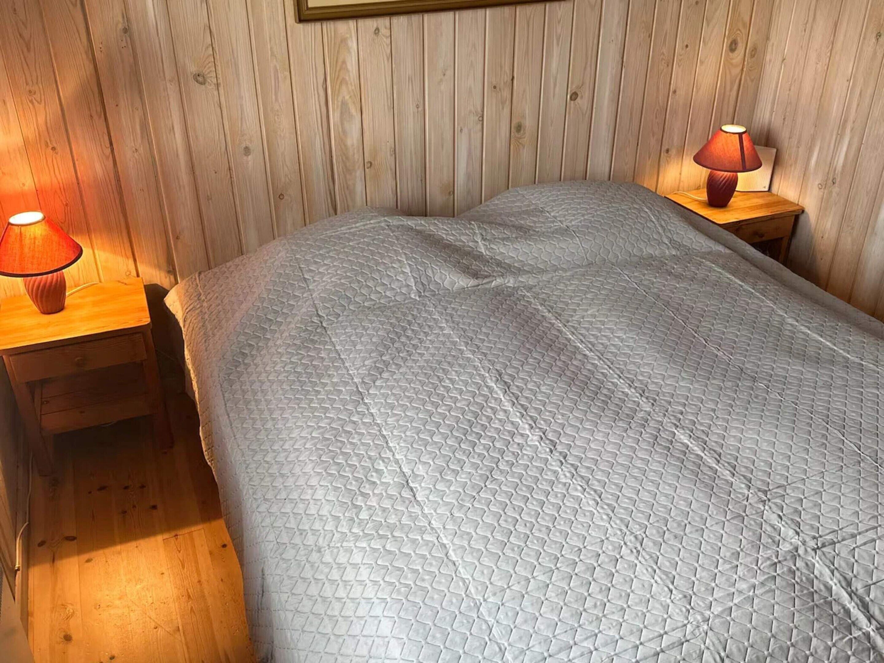 Een kamer met houten lambrisering, een bed, twee nachtkastjes en twee lampen.