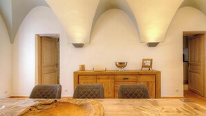 A dining area with a wooden table, three chairs, a wooden buffet, and a high arched ceiling. - A Torra - CATERI - Gîte (CATERI)