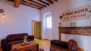 A cozy living room with a wooden ceiling, a sofa, a coffee table, and a fireplace. A sign above the fireplace reads 'A MACAGNA BAR - EPICERIE.' - A Torra - CATERI - Gîte (CATERI)