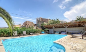 Ein Swimmingpool mit Liegestühlen, einer Hängematte und einer überdachten Sitzgelegenheit.