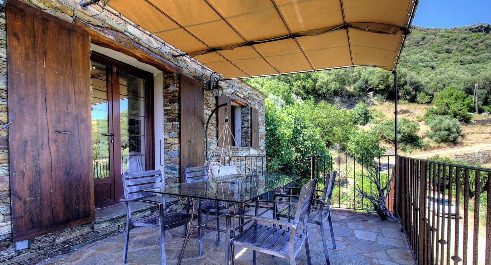 A patio with a glass table and chairs, a wooden door, and a stone wall.