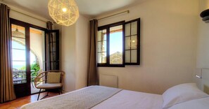 Ein Hotelzimmer mit einem Bett, einem Sessel, einem Fenster mit Aussicht und einer Pendelleuchte.