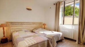 Quarto com duas camas, cabeceira de madeira, janela com cortinas e radiador.